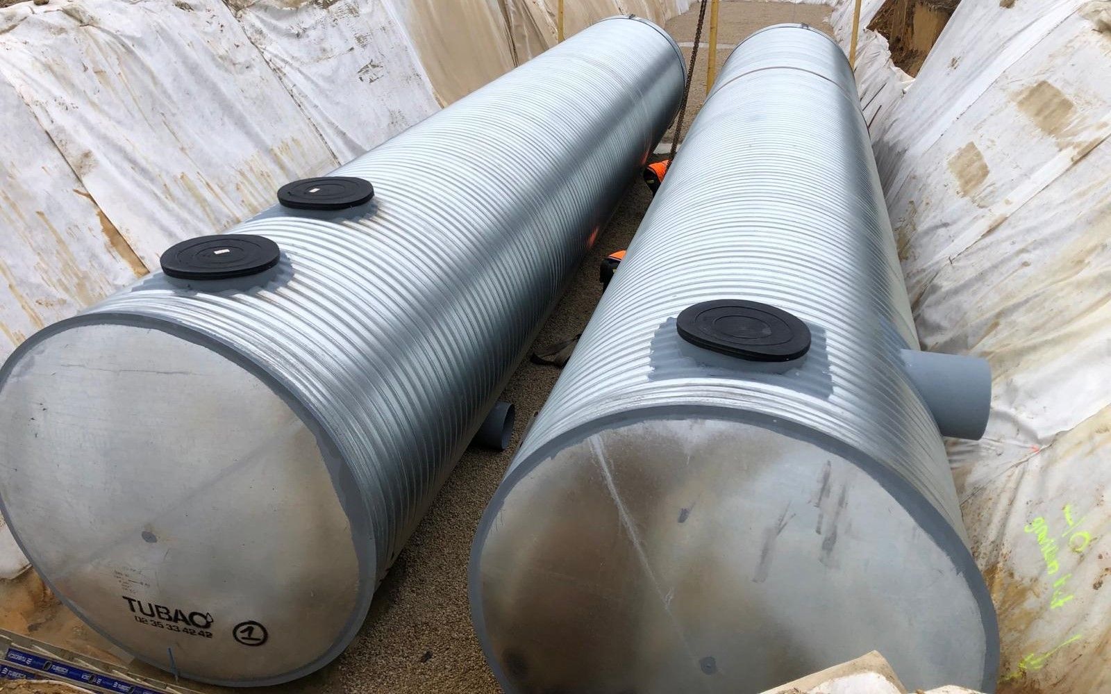 Deux fosses septiques en tôle ondulée installées dans une tranchée, avec les trappes d'accès visibles.