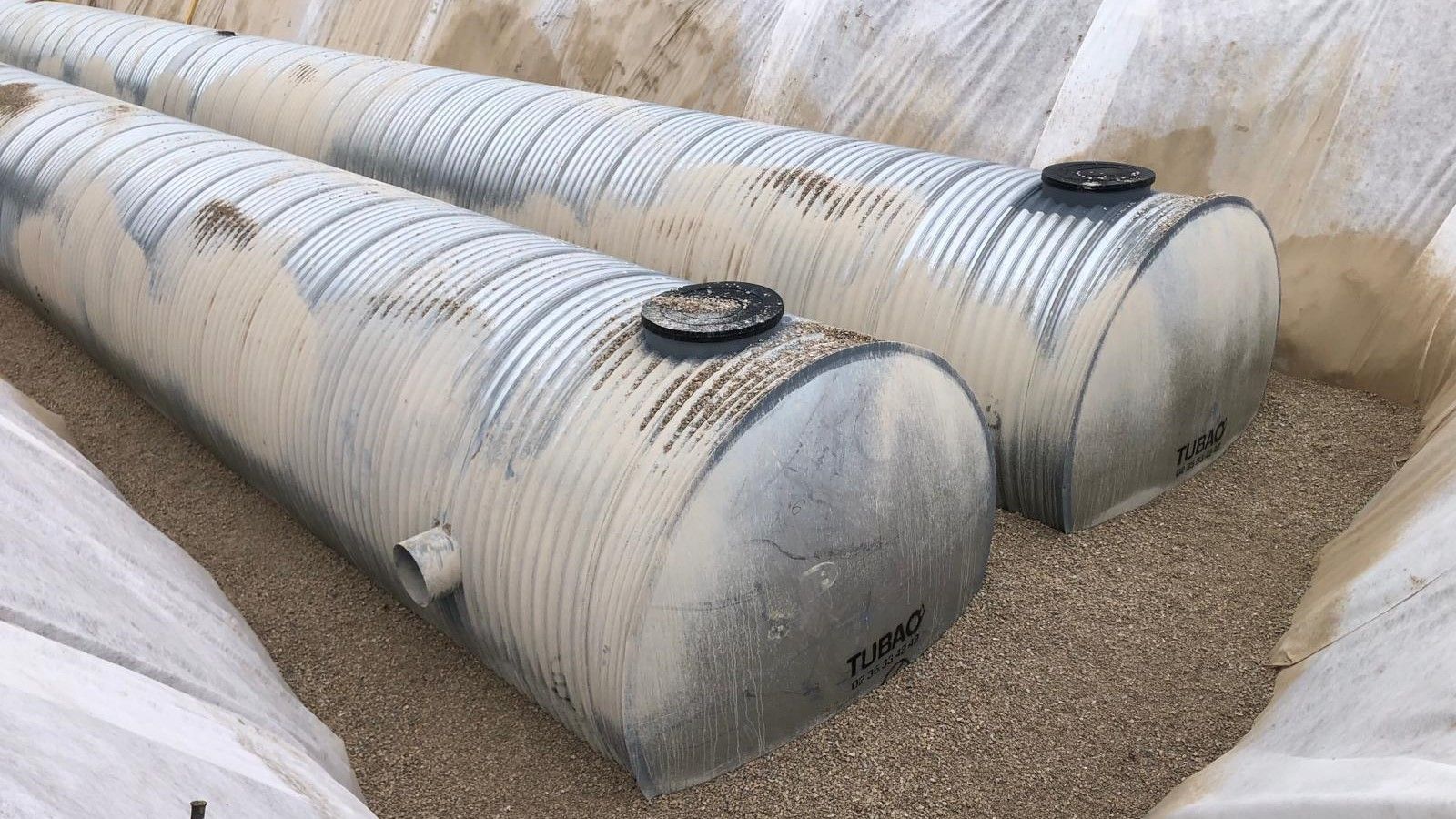 Deux réservoirs en tôle ondulée enterrés dans du gravier à l'intérieur d'une excavation, probablement pour une fosse septique ou du stockage.