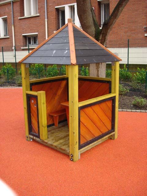 Maisonnette en bois avec des panneaux orange et un toit noir, sur un sol rouge.