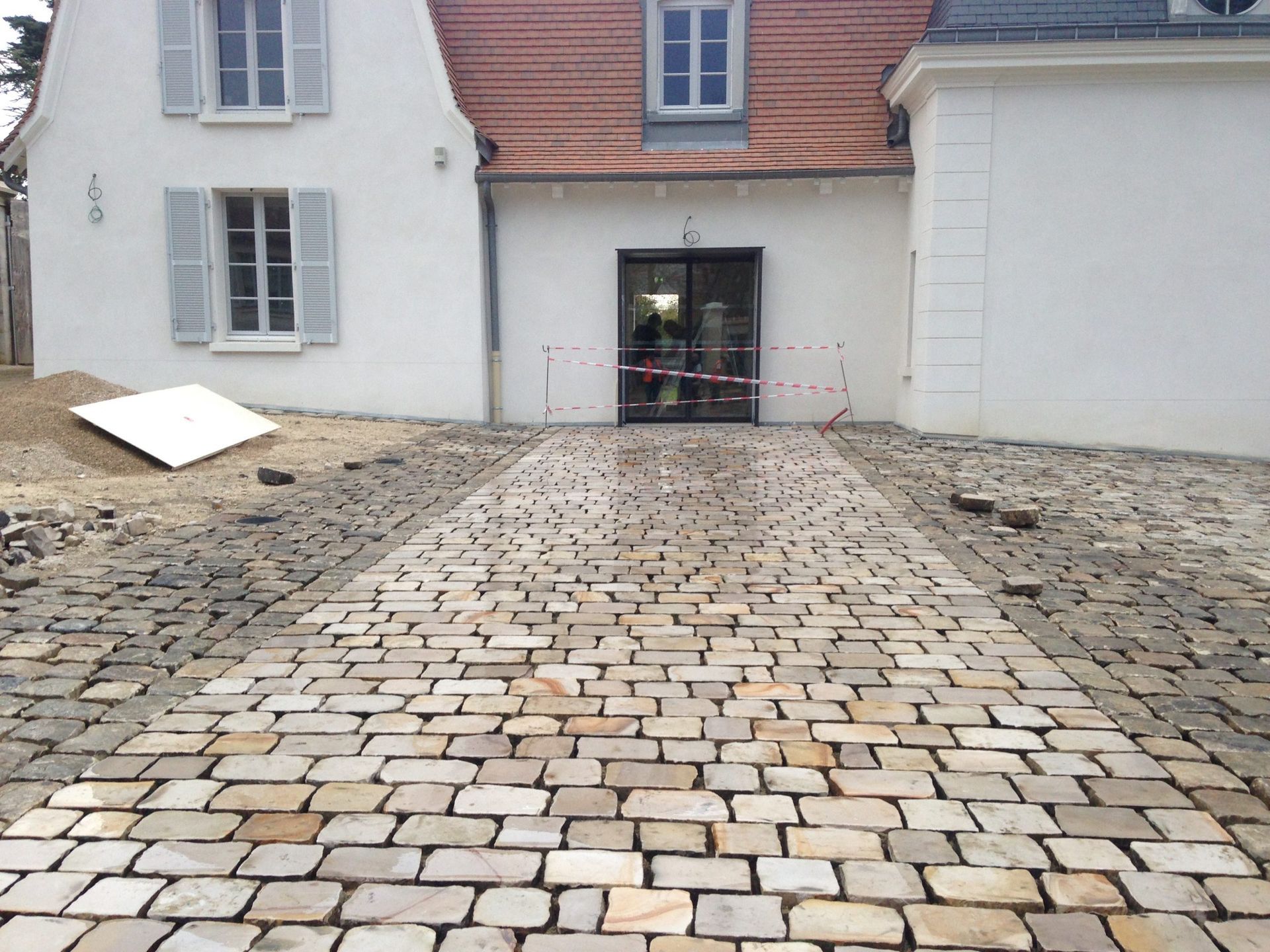 Allée pavée menant à un bâtiment blanc avec des volets et un toit de tuiles rouges.