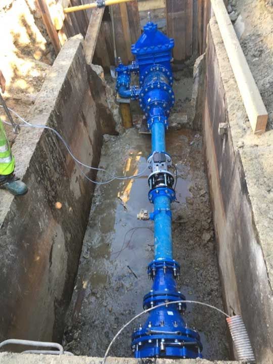 Ensemble de tuyaux d'eau bleus dans une tranchée, entouré de béton et de terre.