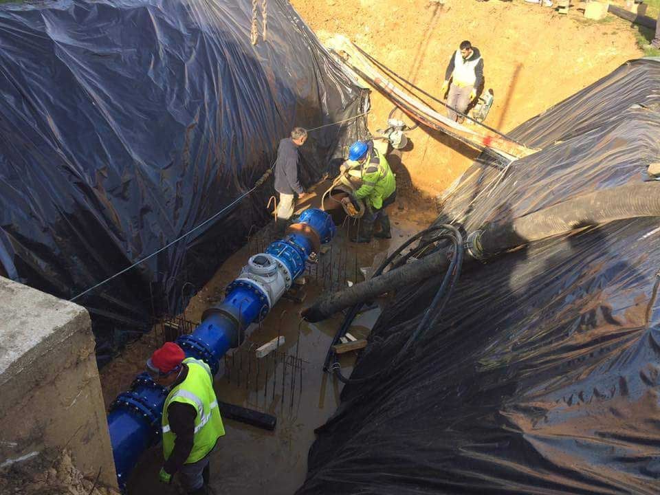 Des ouvriers installent un gros tuyau bleu dans une tranchée tapissée de plastique noir.