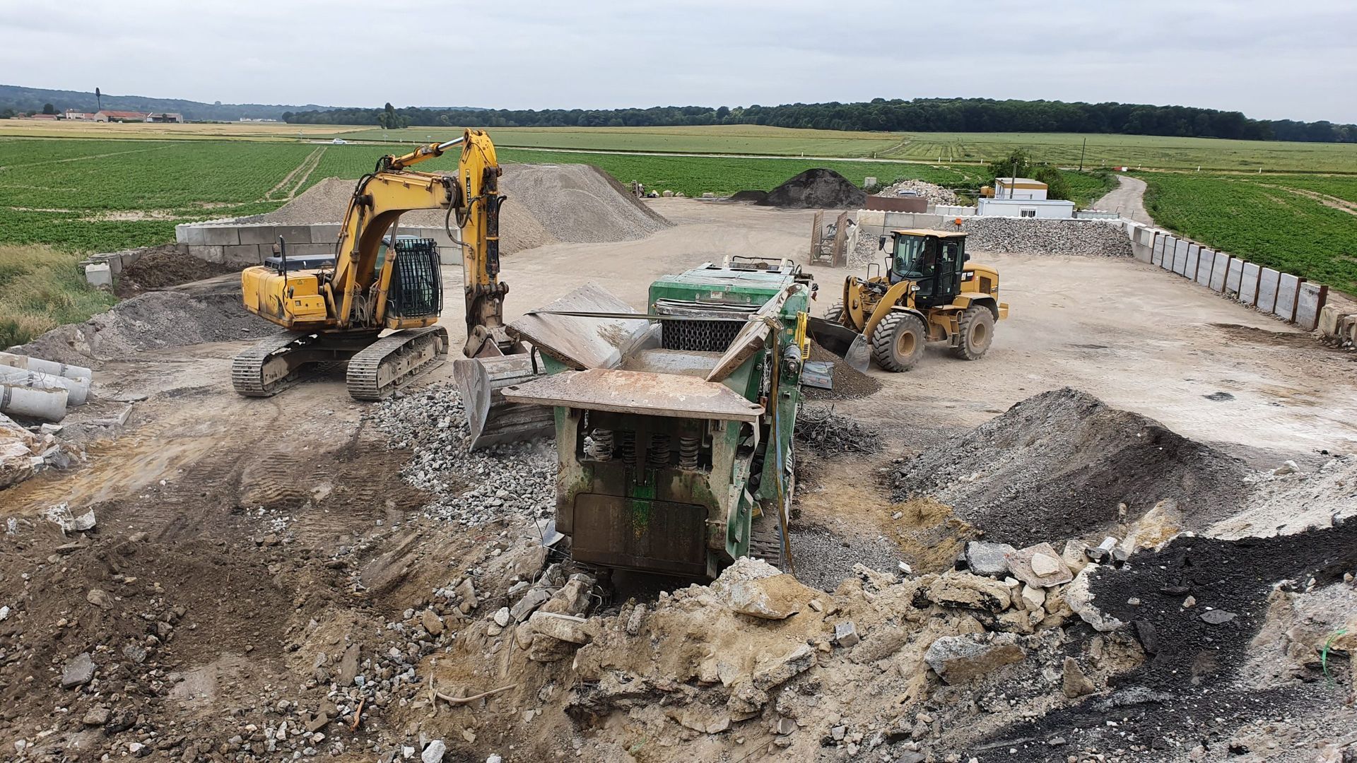 Des engins de chantier lourds démolissent une structure en béton dans un champ.