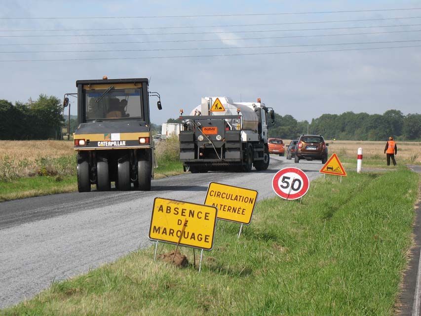 Travaux routiers : Rouleau compresseur et camion sur du nouvel asphalte, panneaux de signalisation, voiture et ouvriers.