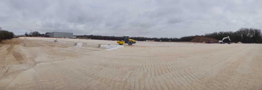 Une machine jaune laboure un champ sous un ciel nuageux.