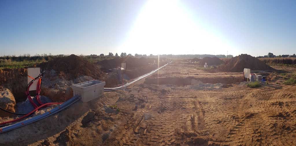 Chantier avec tranchées, conduits et réseaux enterrés. Soleil éclatant dans un ciel dégagé au-dessus d'un terrain terreux.