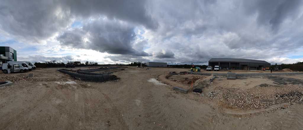 Un vaste chantier sous un ciel nuageux. De la terre, des rochers et des bâtiments au loin.