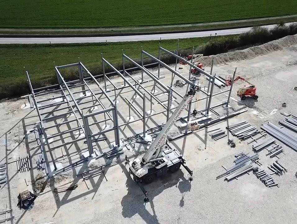 Chantier de construction : structure métallique d’un bâtiment en construction. Grue soulevant des matériaux, entourée de fournitures.