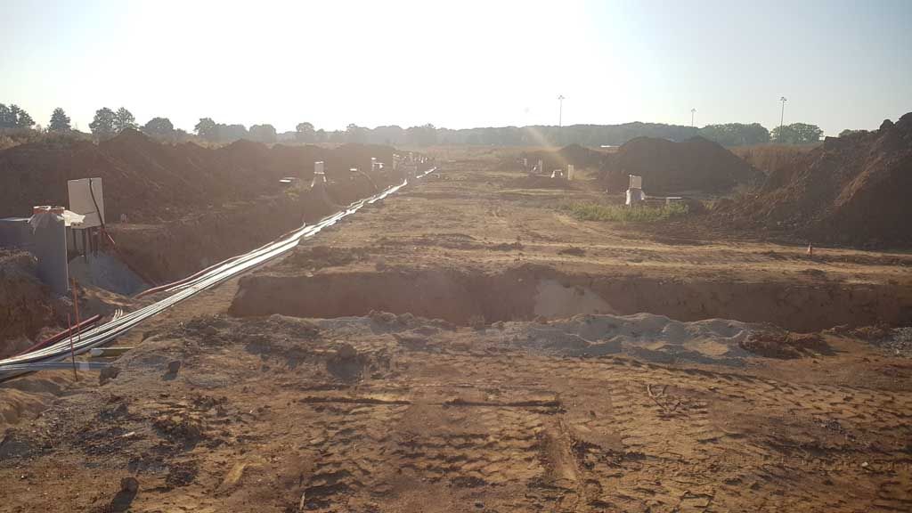 Chantier de construction avec des canalisations apparentes dans une tranchée, bordées de monticules de terre.