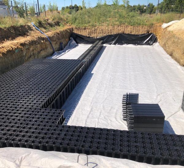 Fosse creusée avec système de grille en plastique noir et revêtement en tissu blanc, prête à être installée.