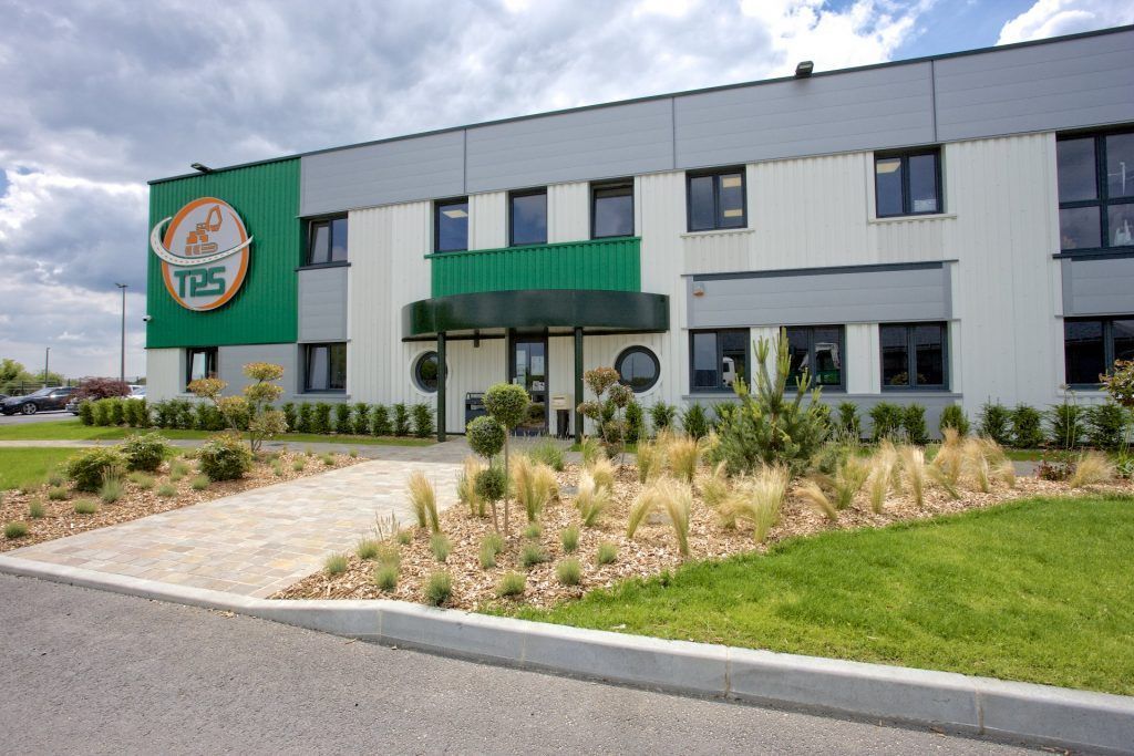 Bâtiment industriel vert et gris avec aménagement paysager et logo « TDS ».