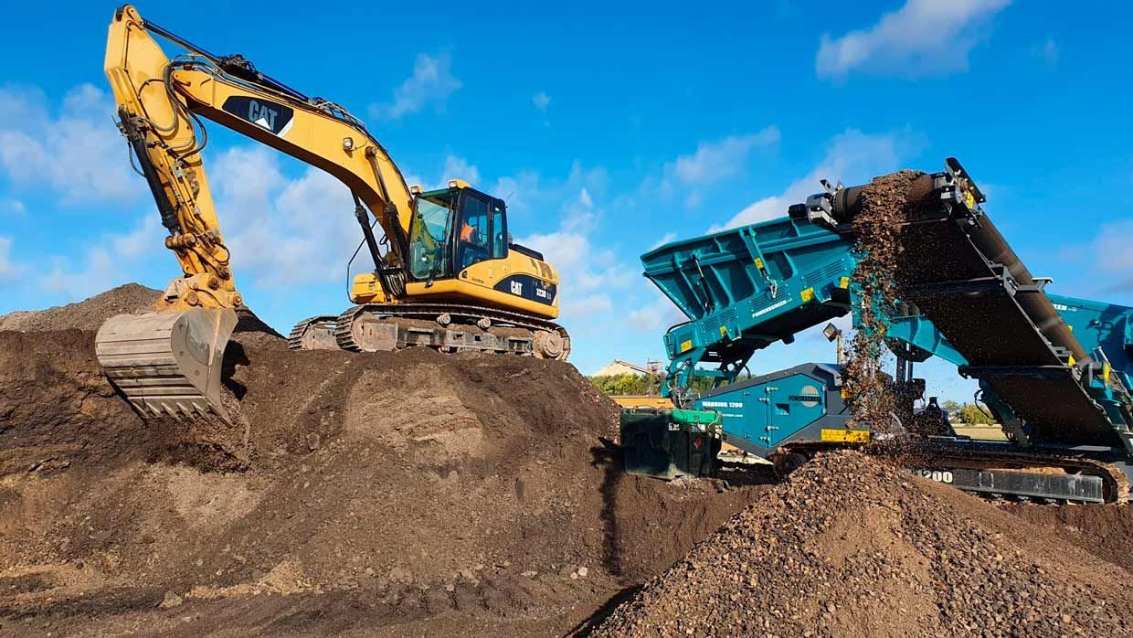 Une excavatrice jaune charge de la terre sur un convoyeur bleu, sous un ciel bleu.