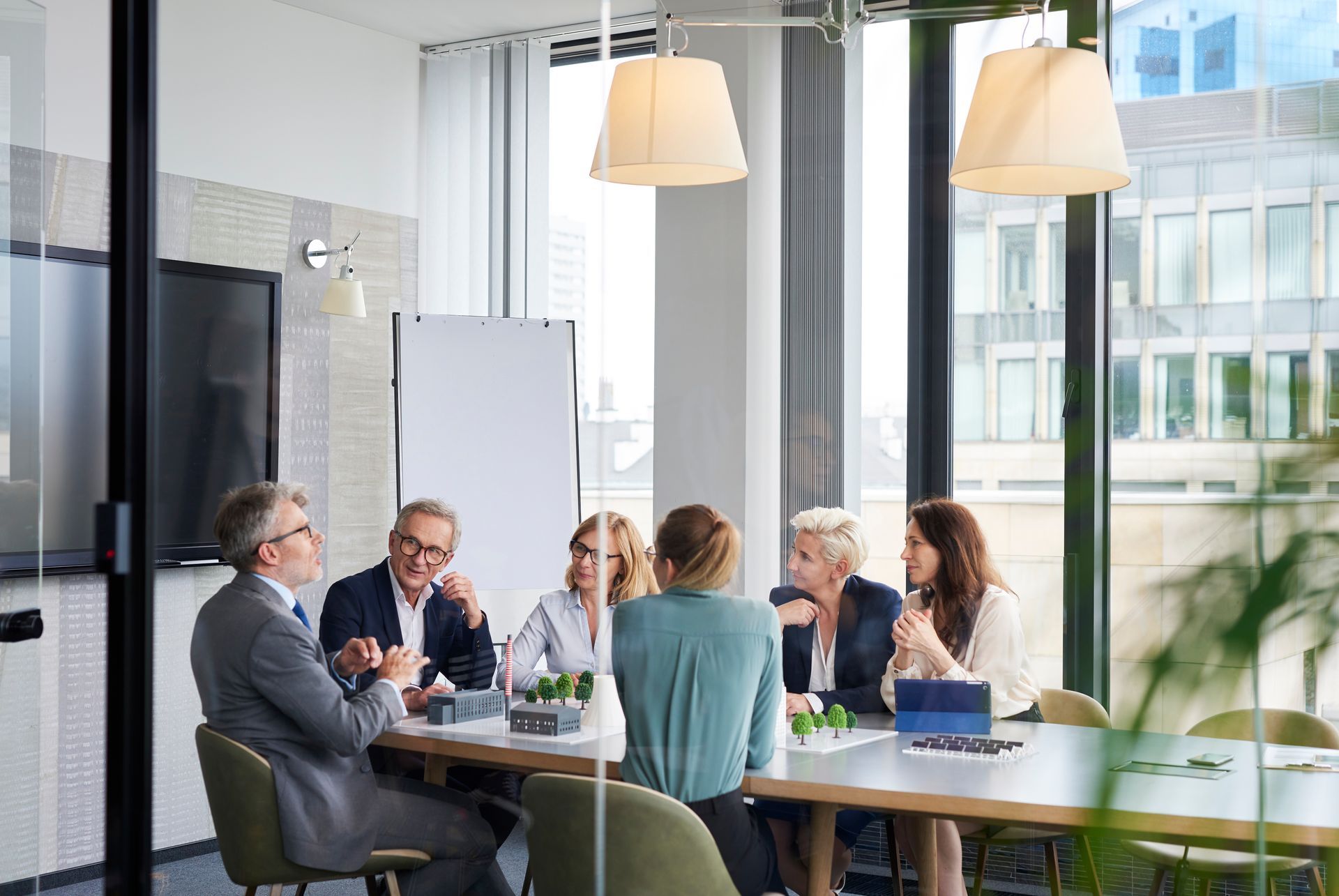 Un groupe diversifié de professionnels en tenue de ville, assis à une table lors d'une réunion dans une salle de conférence aux parois vitrées.