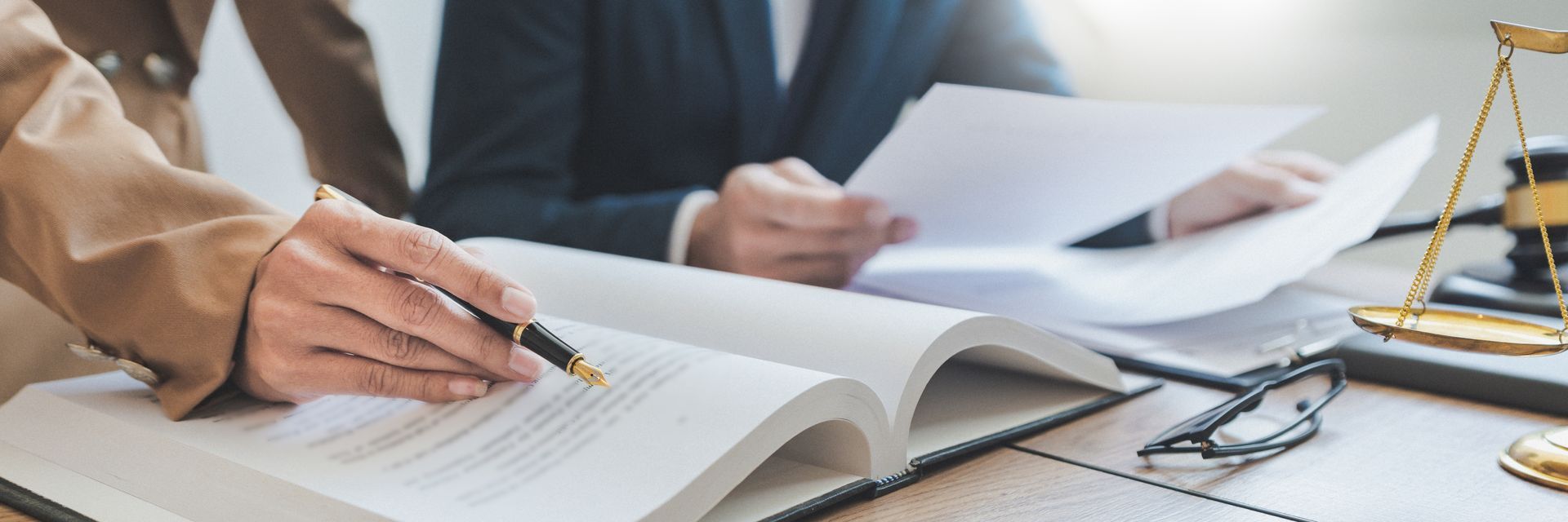 Deux professionnels examinent des documents juridiques et un ouvrage de droit à un bureau où se trouve une balance dorée.