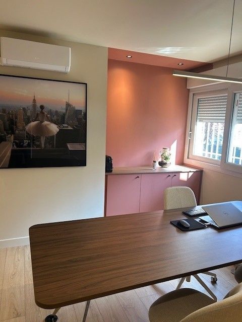 Un bureau à domicile comprenant un bureau en bois, une armoire de rangement rose, un mur rose et une grande reproduction encadrée au mur.
