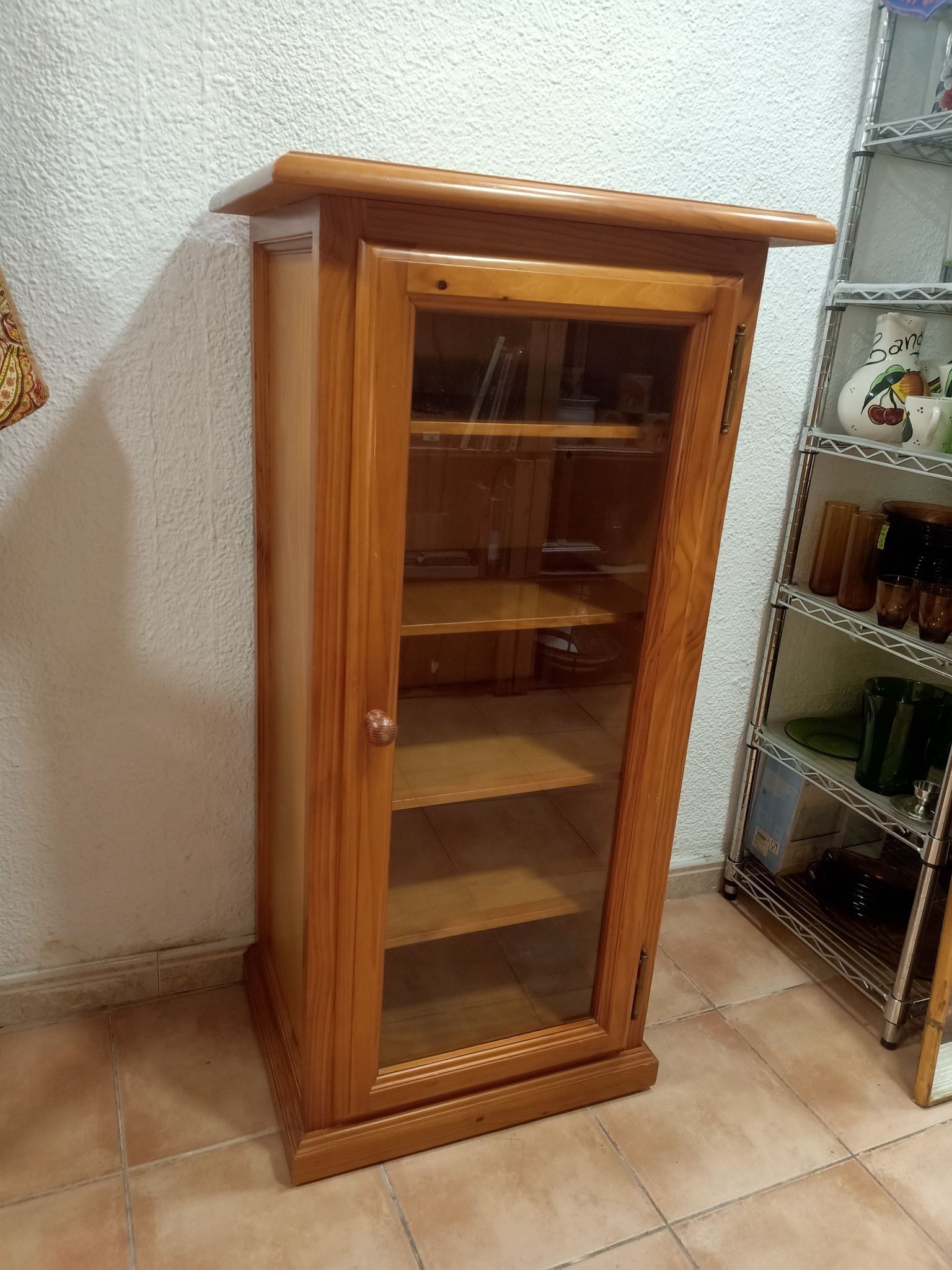 Un armario de madera con puerta de cristal y estantes en una habitación.