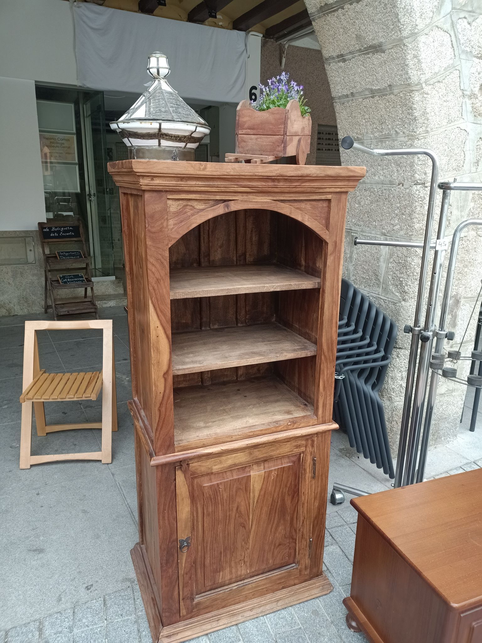 Un armario de madera con estantes y un frasco de vidrio encima.