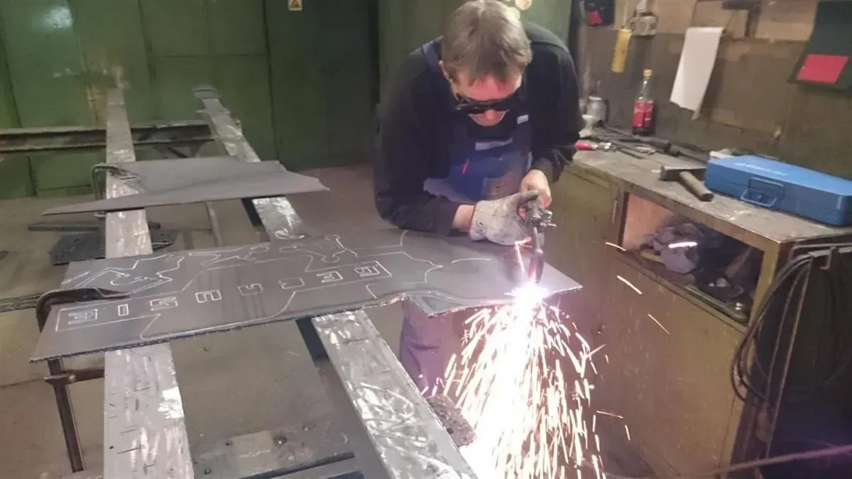 Mann schneidet in einer Werkstatt Metall mit einem Plasmaschneider, Funken fliegen.