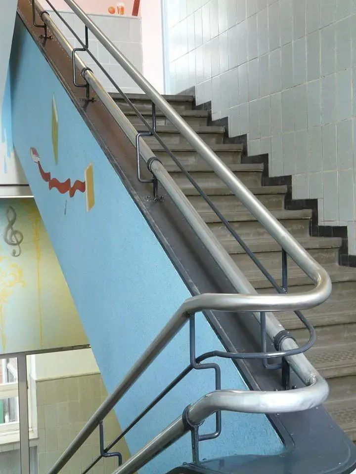 Treppe mit Metallhandläufen, blaue Wand mit Verzierungen.