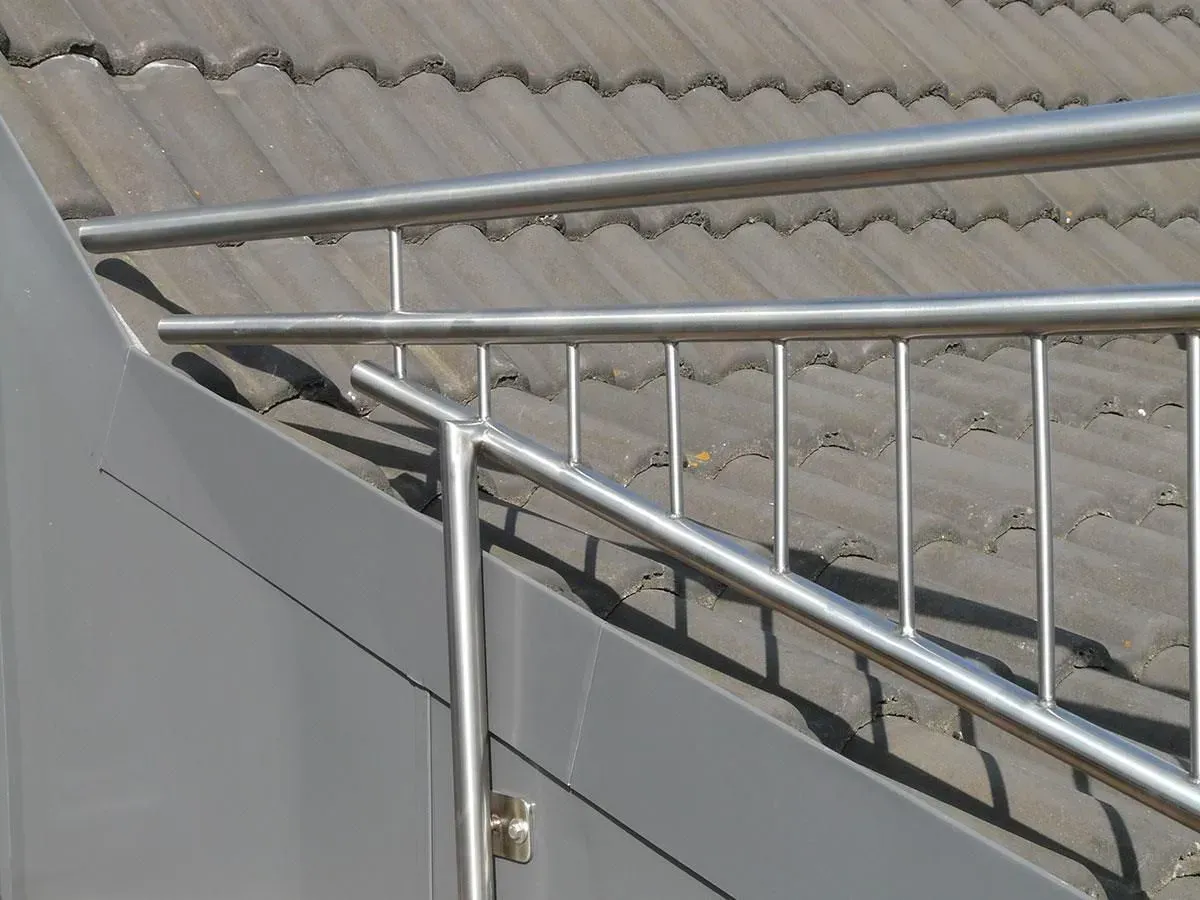 Metallgeländer an einem grauen Gebäude, im Hintergrund ein Ziegeldach.