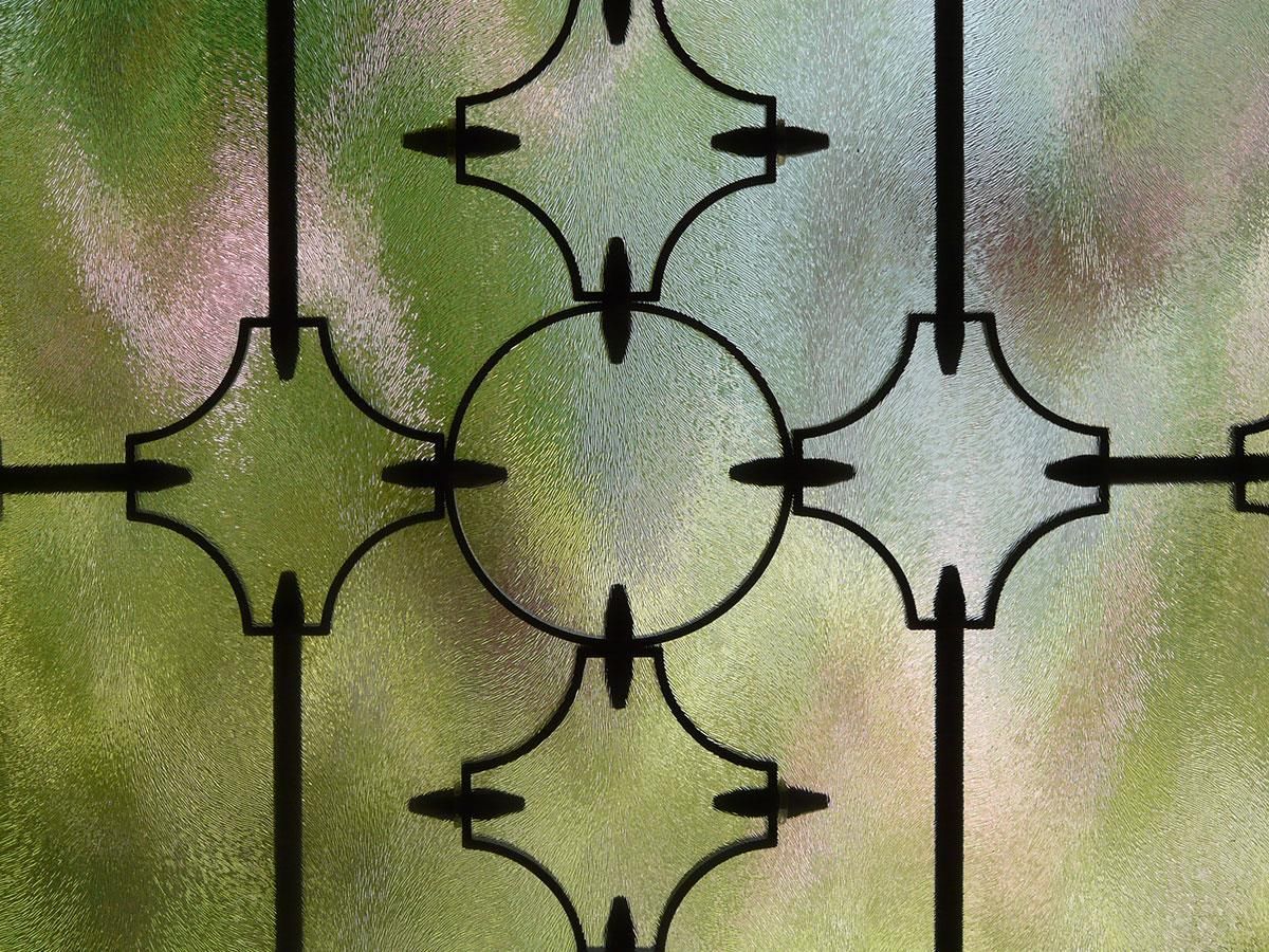 Schwarzes dekoratives Metallfenster mit Milchglas, unscharfer grüner Hintergrund.