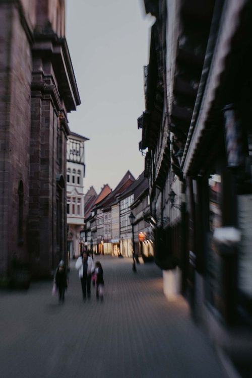 Ein verschwommenes Bild einer Stadtstraße mit Gebäuden und Menschen, die sie entlanggehen.