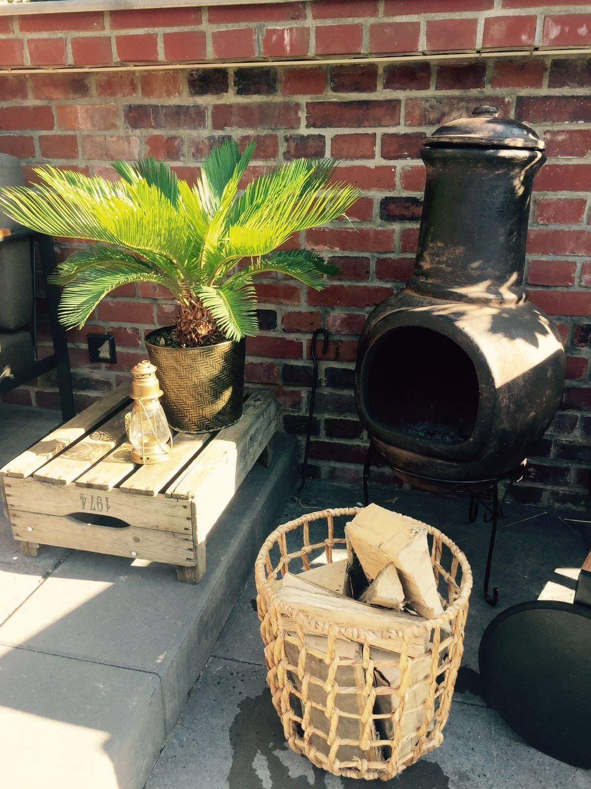 Neben einer Backsteinmauer steht ein mit Holzscheiten gefüllter Korb.