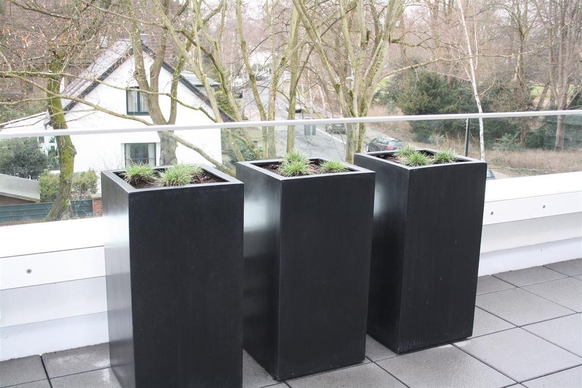 Auf einem Balkon stehen drei schwarze Pflanzgefäße.