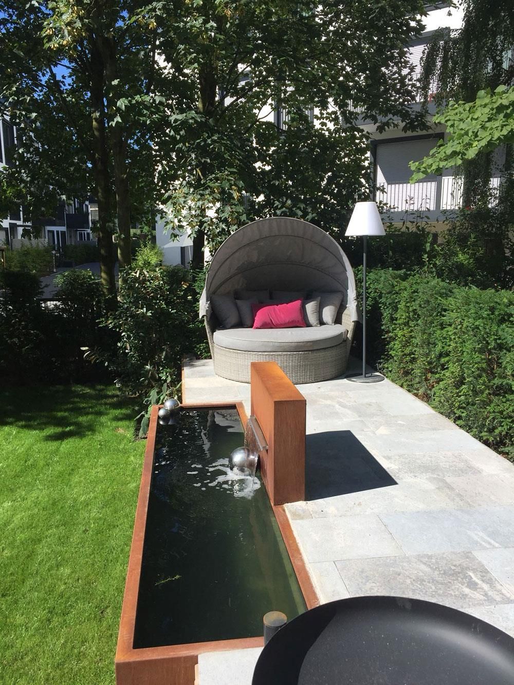 Neben einem Teich in einem Garten steht ein rundes Sofa.