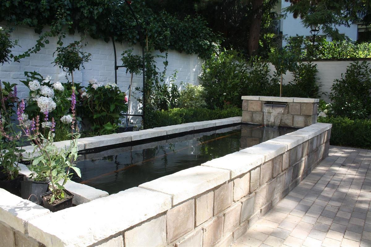 Eine Backsteinmauer umgibt einen großen Teich in einem Garten