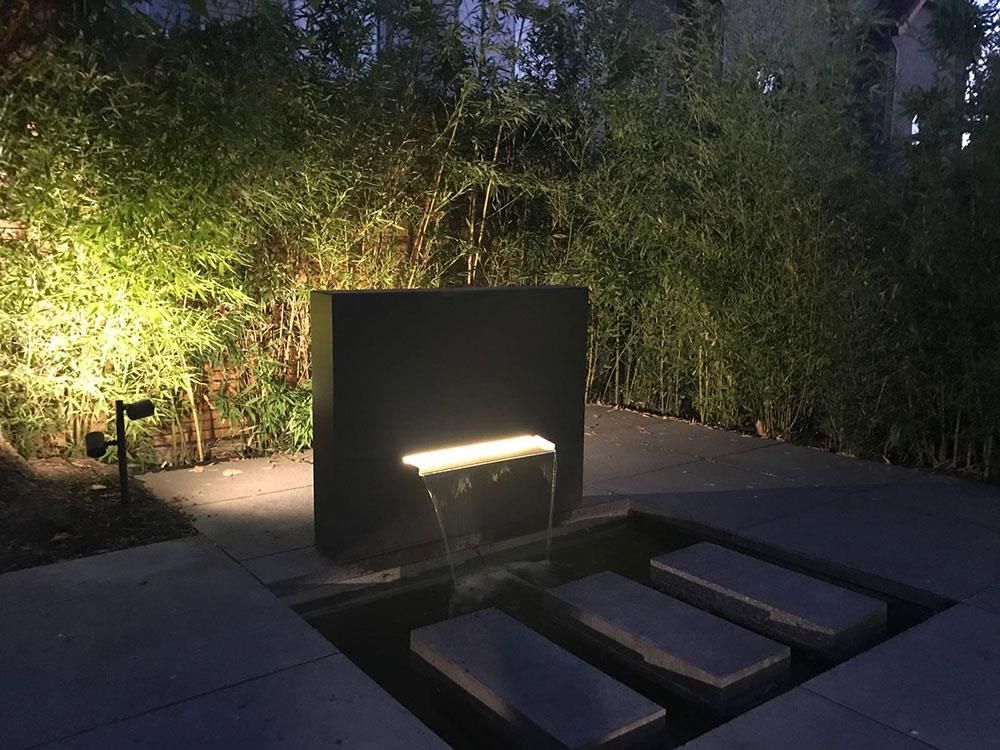 In einem von Bäumen umgebenen Garten ist nachts ein Wasserfall beleuchtet.