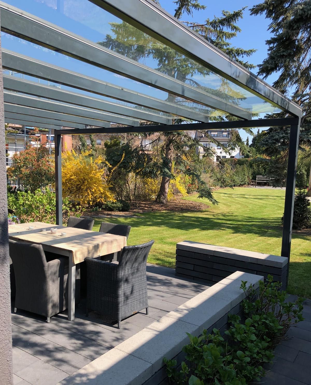 Eine Terrasse mit Tisch und Stühlen unter einem Glasdach.