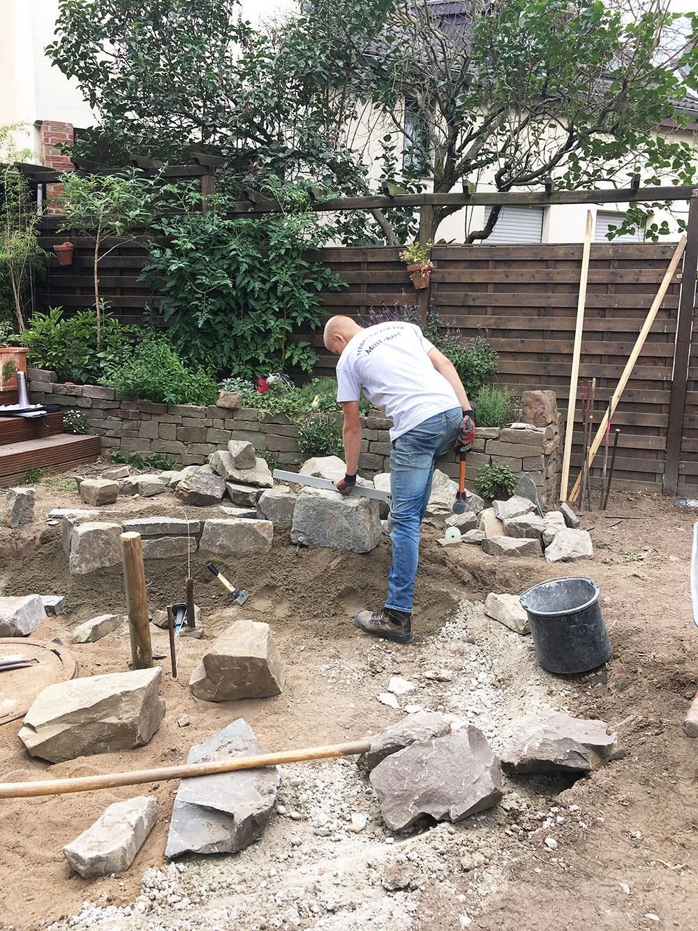 Ein Mann arbeitet in einem Hinterhof an einer Felsmauer.