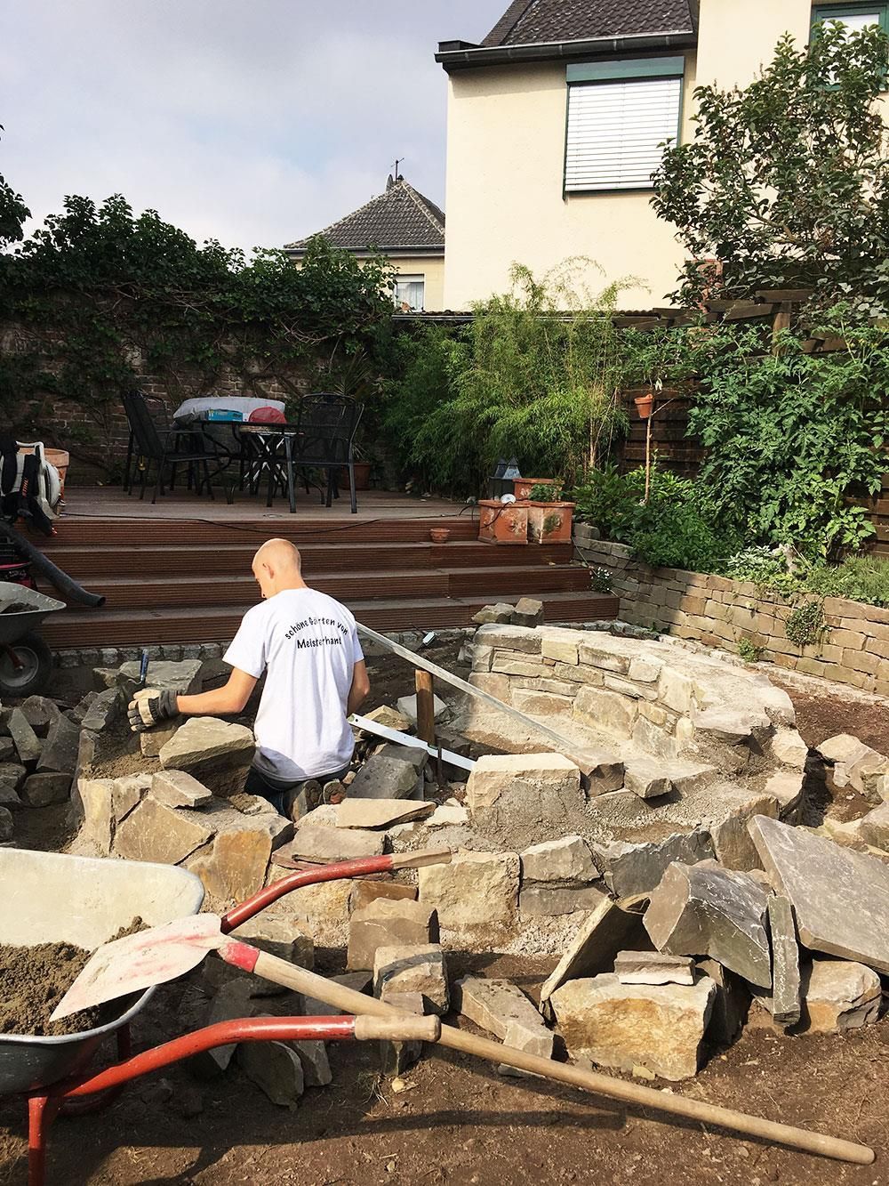 Ein Mann sitzt auf einem Steinhaufen neben einer Schubkarre.