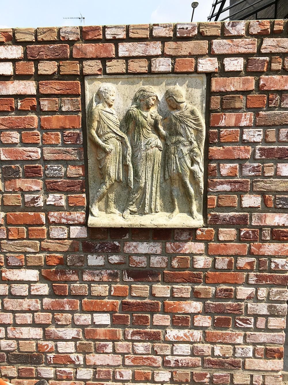 Eine Backsteinmauer mit einer Statue von drei Personen darauf.