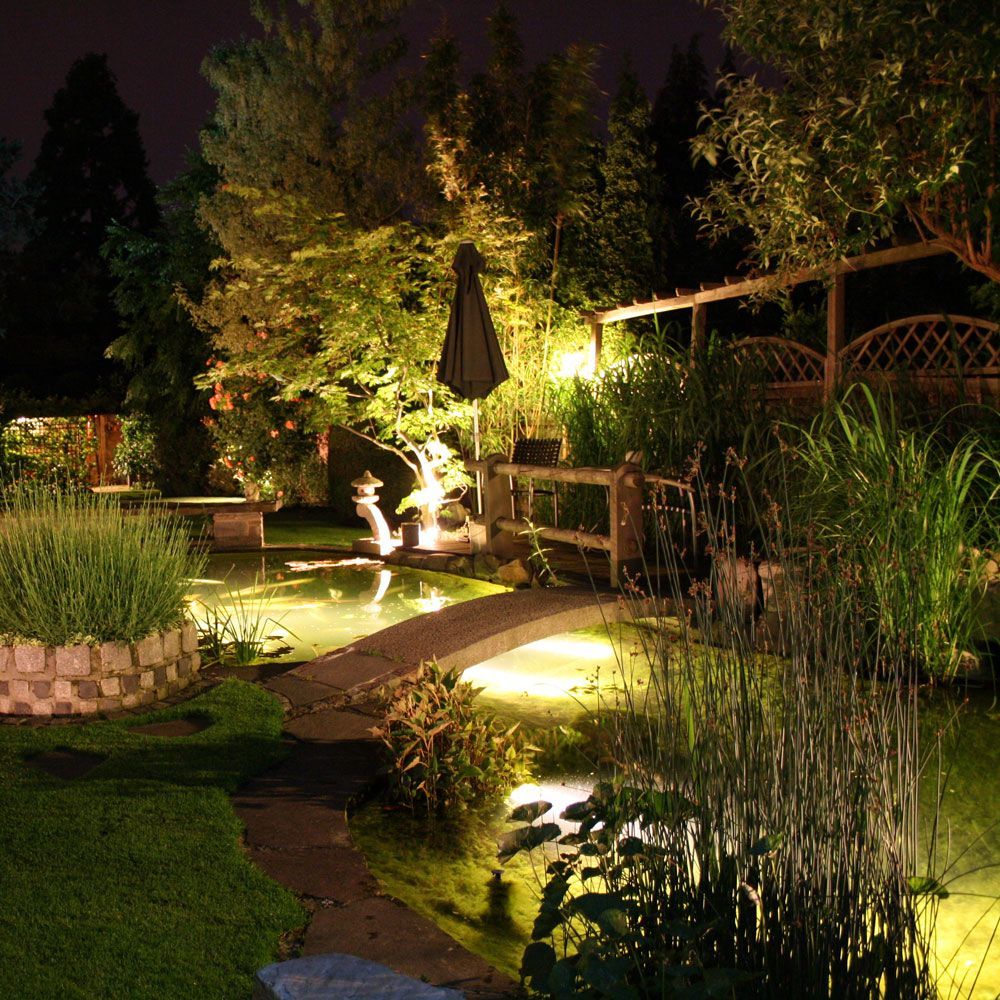 Ein Garten mit einem Teich und einer Brücke bei Nacht