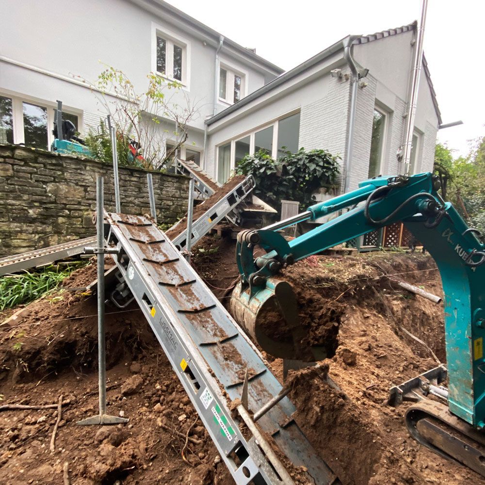 Ein Bagger gräbt vor einem Haus ein Loch in den Boden.