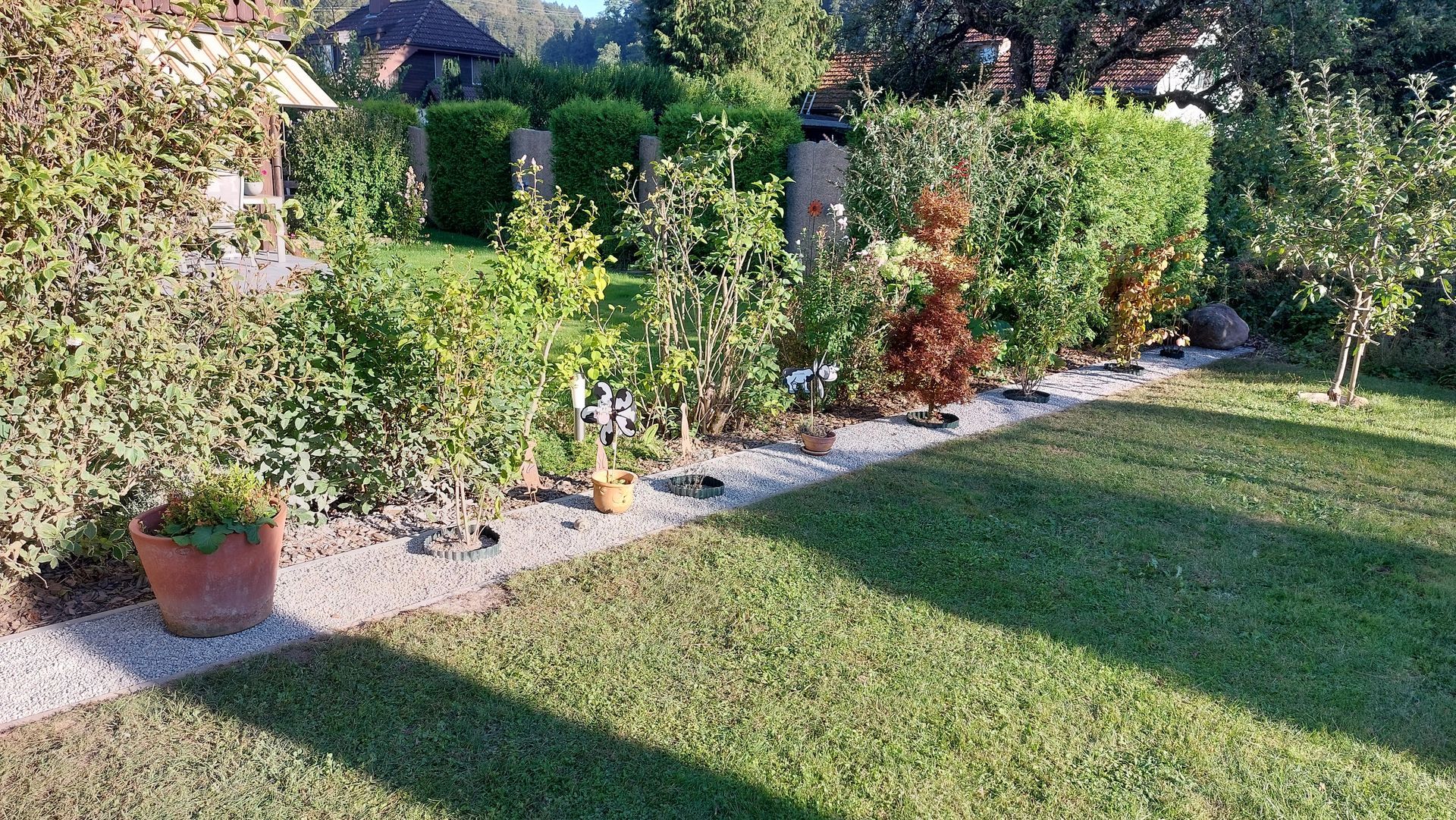 Ein Maler in Overalls streicht mit einer Farbrolle eine weisse Wand in einem Zimmer; links davon steht eine Leiter.