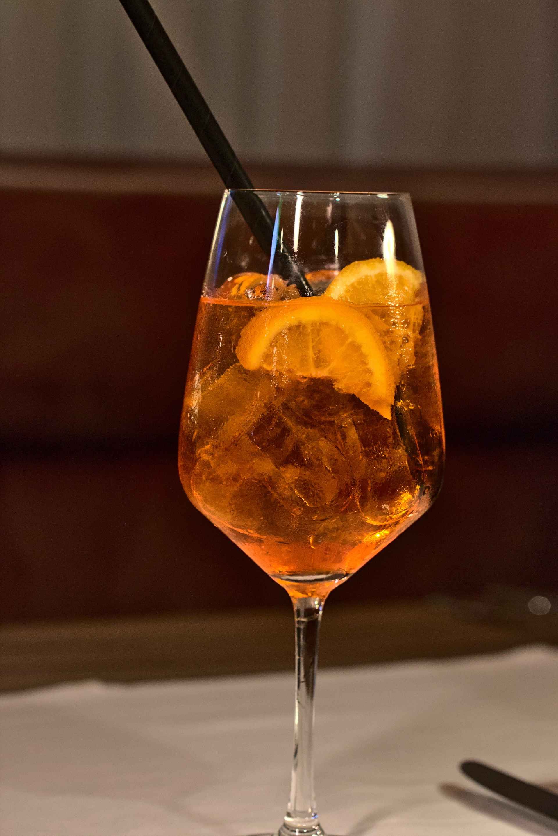 Orange Aperol Spritz in einem Stielglas mit Orangenscheibe und schwarzem Strohhalm.