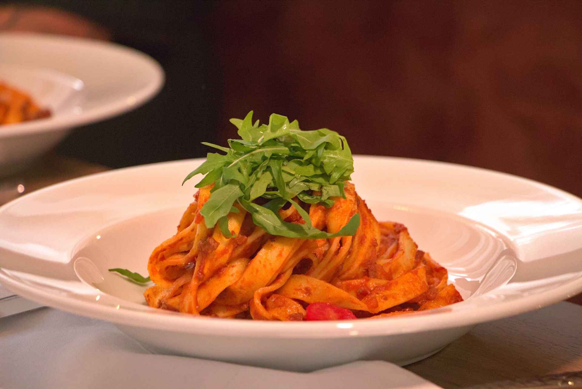 Pastagericht mit roter Sosse, garniert mit grünem Rucola, in einer weissen Schüssel.
