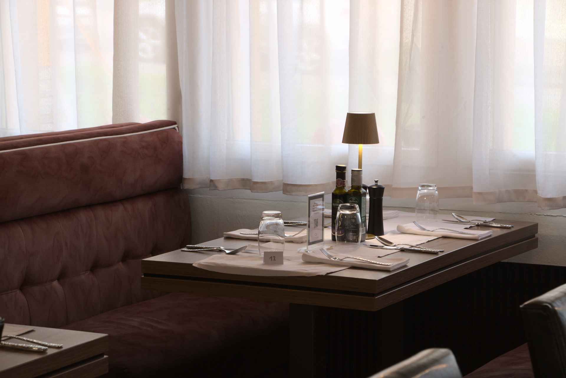 Restaurantsitzgruppe mit gedecktem Tisch, Lampe und transparenten Vorhängen.