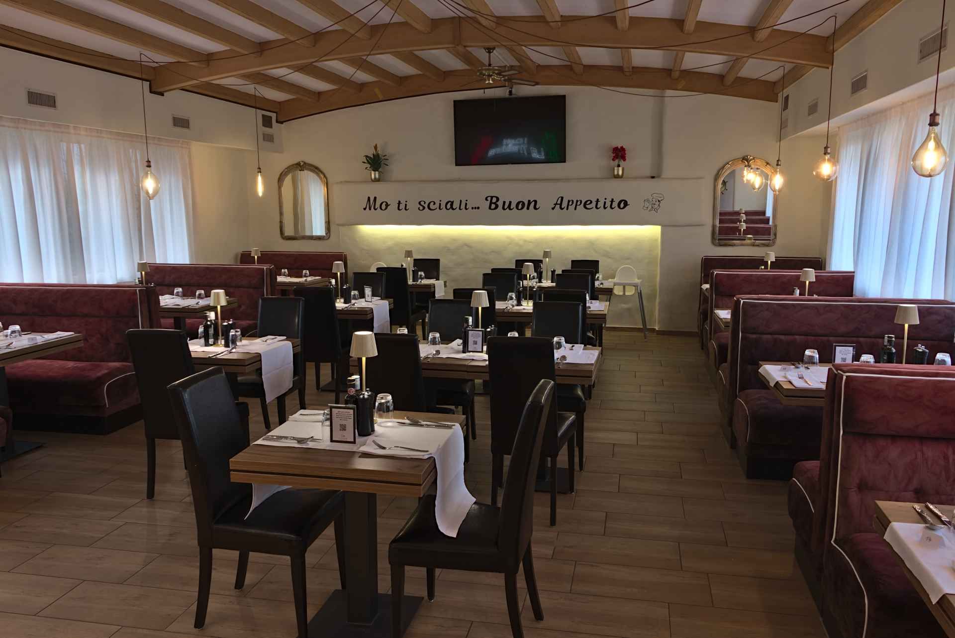 Restaurantinterieur mit gedeckten Tischen, roten Sitznischen und dekorativer Beleuchtung.
