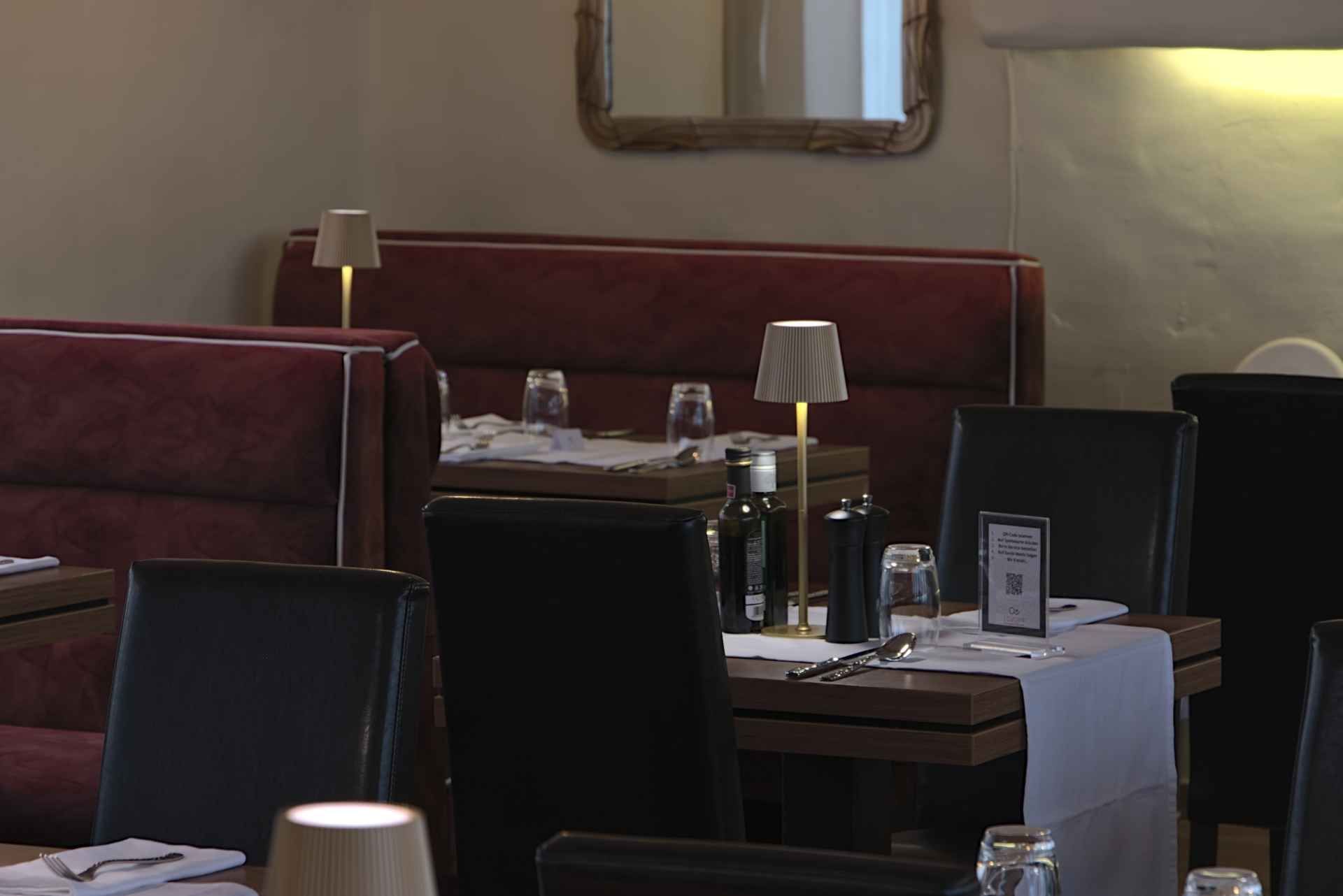 Restaurant-Essbereich mit roten Sitznischen, schwarzen Stühlen und Tischen, die mit Lampen und Gläsern gedeckt sind.