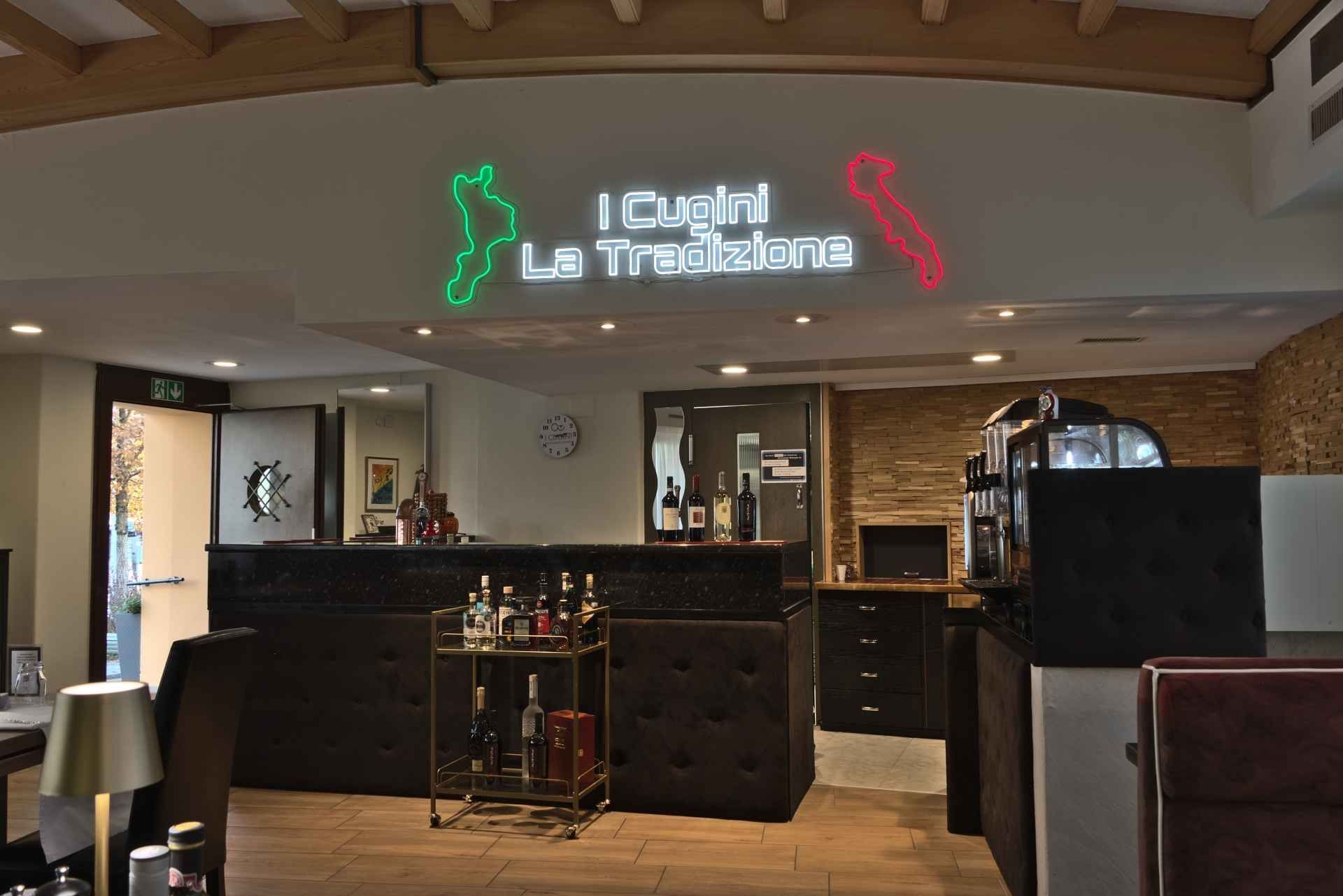 Interieur eines italienischen Restaurants mit einer Leuchtreklame, die eine Karte von Italien und den Text „I Cuochi La Tradizione“ zeigt.