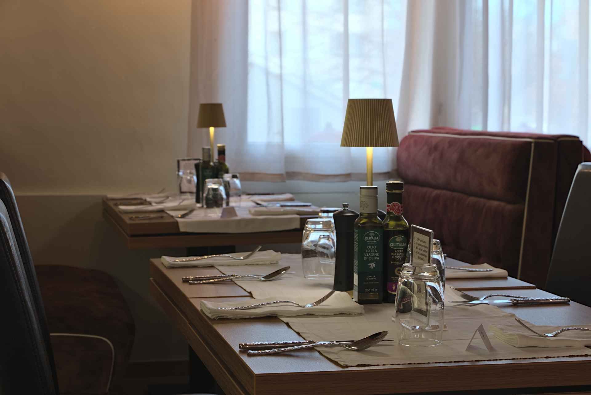 Ein zum Essen gedeckter Restauranttisch mit Servietten, Besteck und Gläsern. Zwei Lampen beleuchten die Szene.