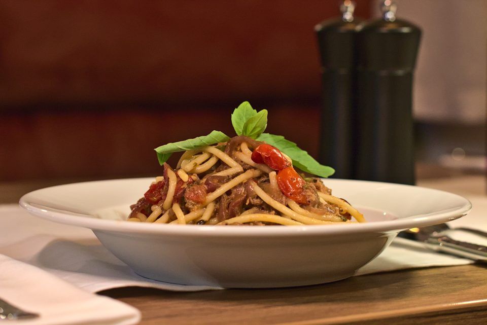 Pastagericht mit Fleischsosse und Basilikumgarnitur, serviert in einer weissen Schüssel, im Hintergrund sind Pfeffermühlen zu sehen.