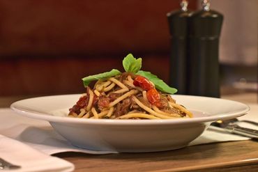Pastagericht mit Fleischsosse und Basilikumgarnitur, serviert in einer weissen Schüssel, im Hintergrund sind Pfeffermühlen zu sehen.