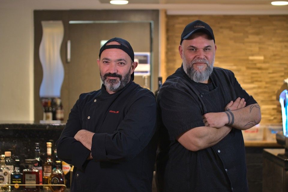 Zwei Köche in schwarzen Uniformen, die Arme verschränkt, stehen in der Nähe einer Bar, Restaurantatmosphäre.