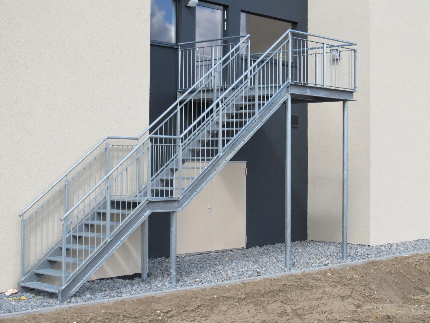 An einem Gebäude befestigte Außentreppe aus Metall, die zu einem Treppenabsatz führt.