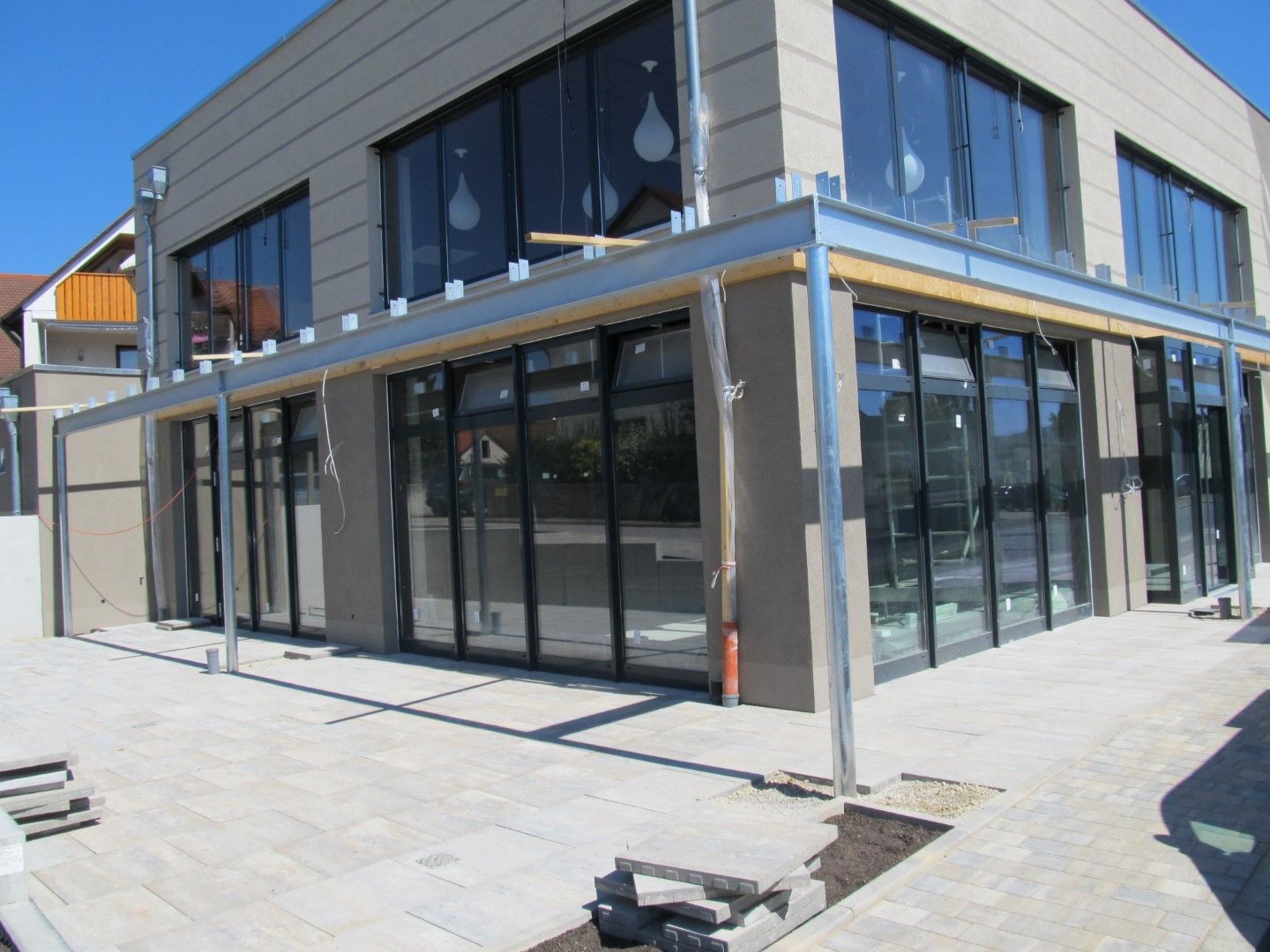 Gebäudeaußenseite mit großen Fenstern und einer Metallmarkise; Außenterrasse im Bau.